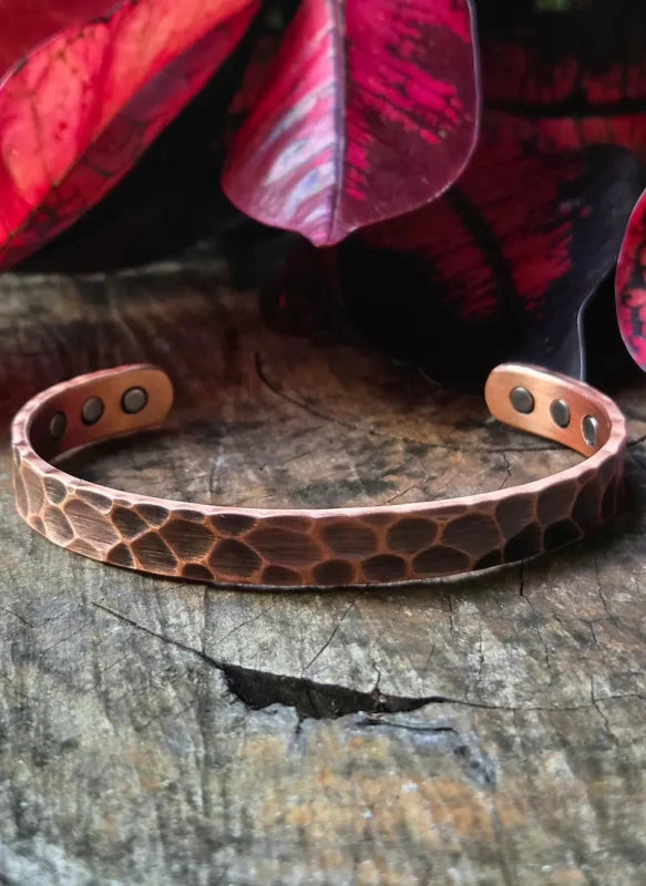 Copper bracelet with a textured hammered pattern on a wooden surface with red leaves in the background