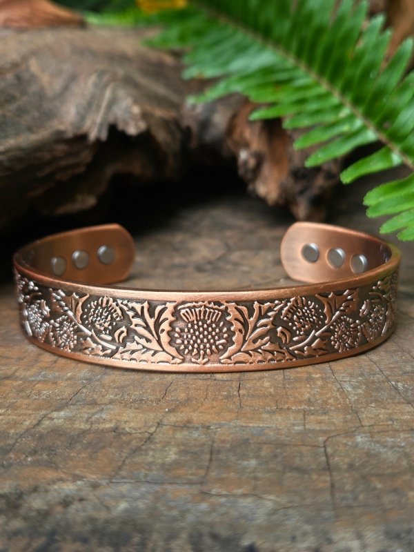 Copper bracelet with floral patterns on a wooden surface with fern leaves in the background