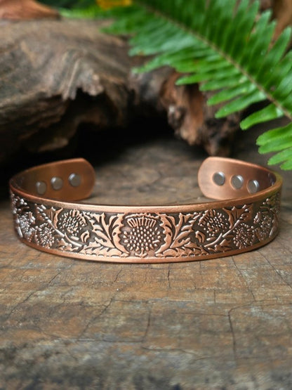 Copper bracelet with floral patterns on a wooden surface with fern leaves in the background