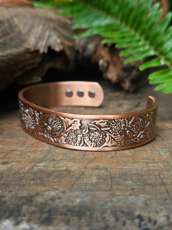 Copper bracelet with floral patterns on a wooden surface with ferns in the background