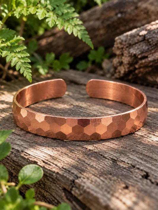 Copper hammered bracelet on a wooden surface with green leaves in the background