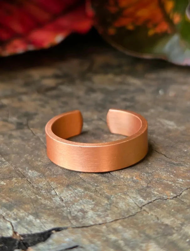 A copper ring resting on a textured stone surface with blurred leaves in the background.