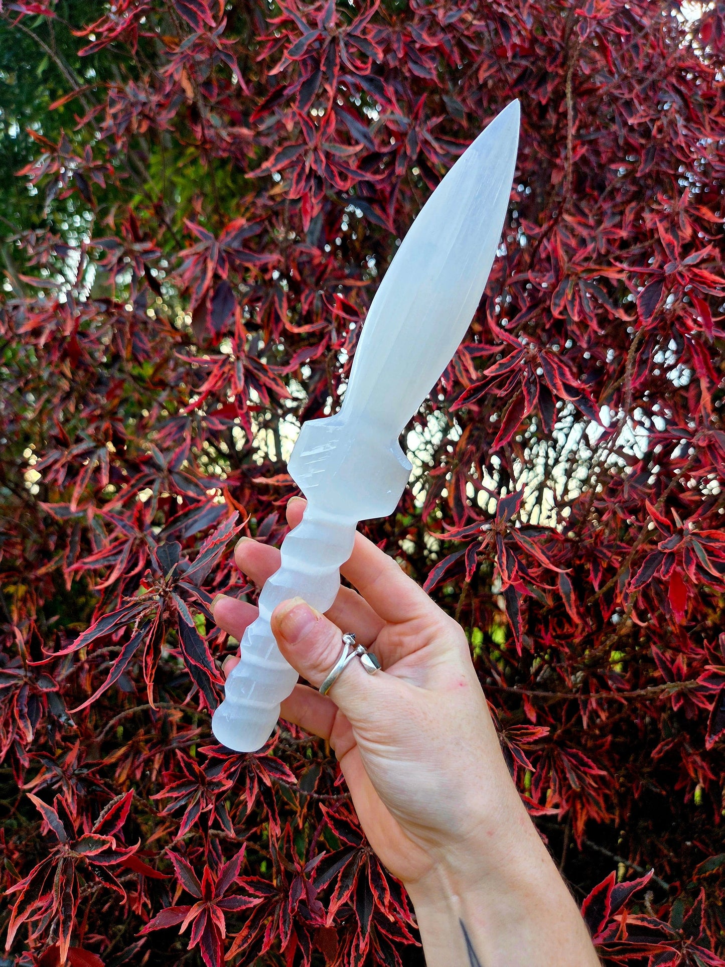 Hand holding a white crystal dagger knife against a red and green leafy background